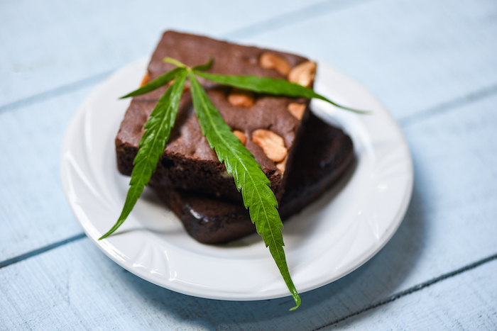 The benefits of cooking with Cannabis at Pure Life Wellness in Baltimore | brownies with cannabis leaf marijuana herb on white plate background - cannabis food snack for health